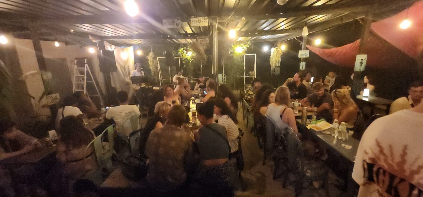 The bar at night, full, under string lights and a corrugated roof